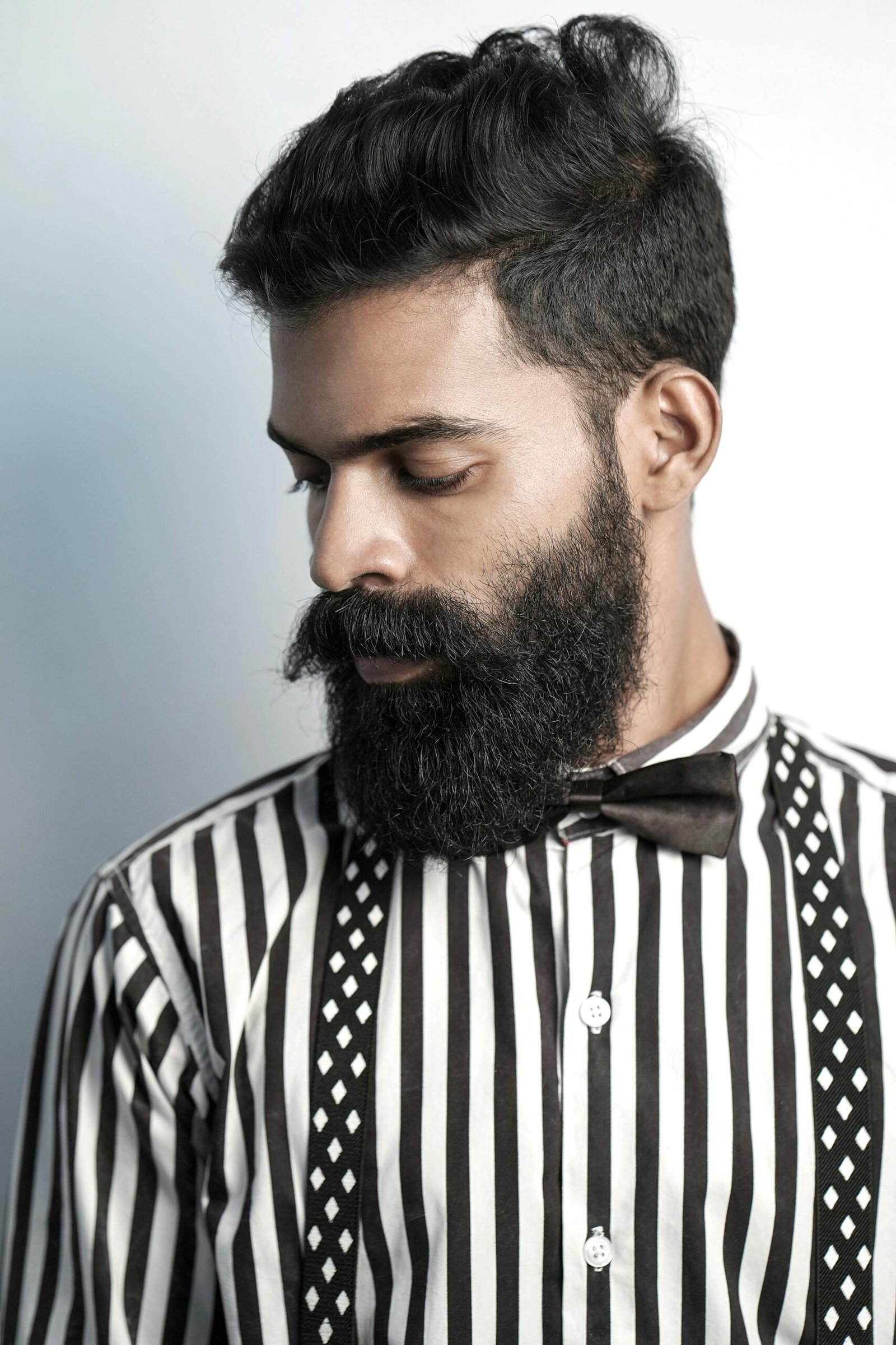 Portrait of a stylish South Asian man with a beard and mustache, wearing a striped shirt and bow tie.